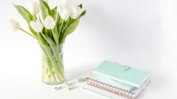 white tulips in a vase and a turquoise diary on a table