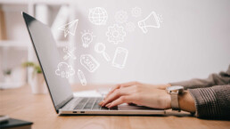 person typing on a laptop while ghostly business words and pictures appear above the keyboard